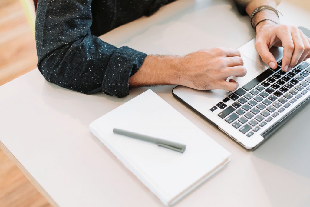 Person Communicating Online via a Laptop with Notebook and Pen